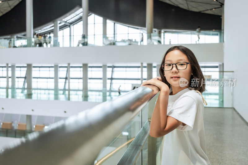 戴眼镜女孩在现代建筑内扶栏杆