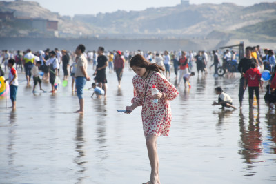 女子在热闹海滩赤脚行走