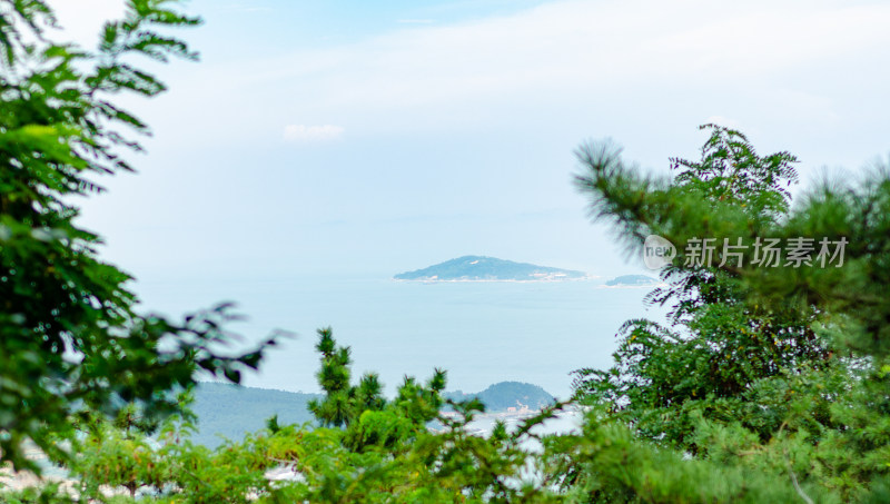 青岛崂山仰口景区，透过重叠的树看远处海岛