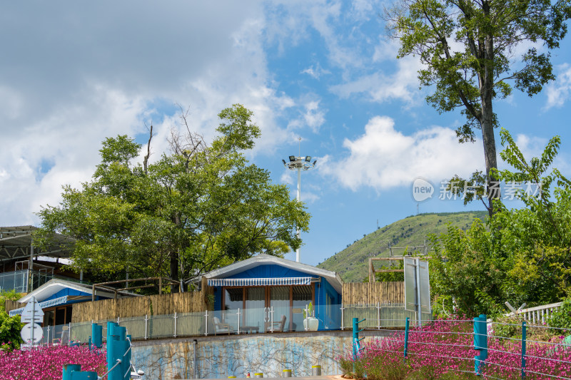 户外蓝顶小屋景观，周边绿树繁花环绕