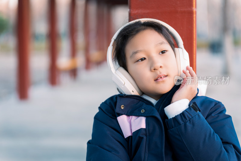 冬日暖阳坐在公园长廊带耳机欣赏音乐的女孩