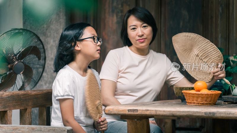 母女俩在古旧桌边拿着扇子的生活场景