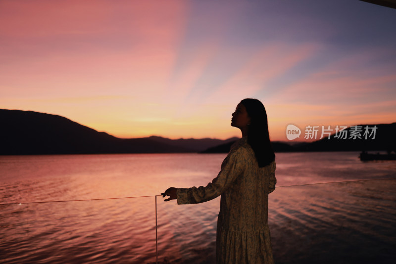 日落时站在湖边的女人的侧视图