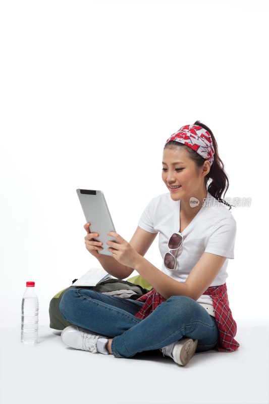 棚拍户外旅行的年轻女人坐在地上玩平板电脑