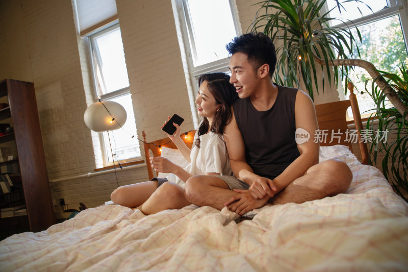 青年情侣坐在床上看手机