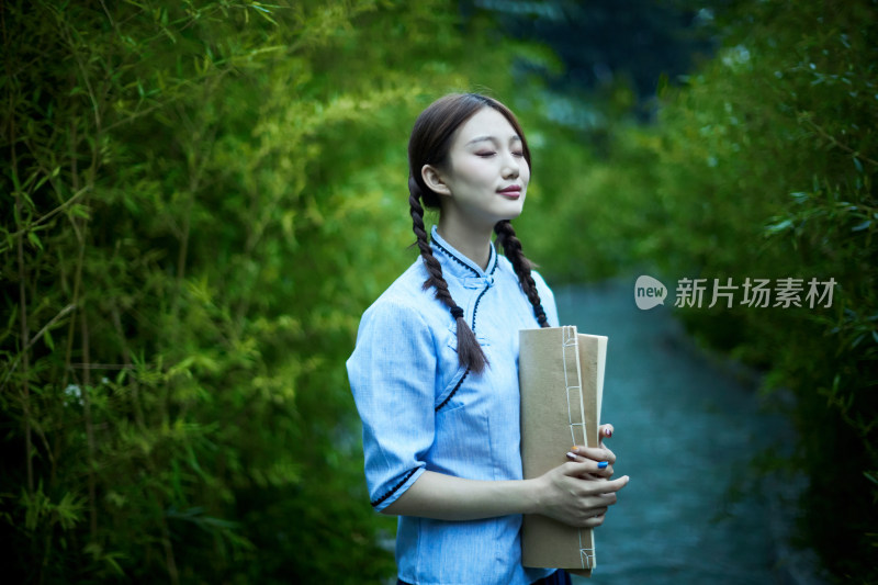 细雨中庭院里竹林前怀抱古书籍的民国风少女