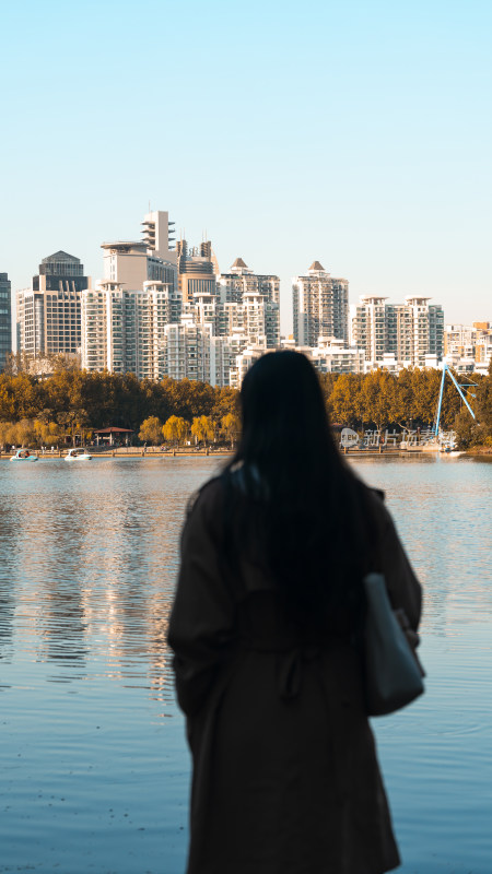 女子背影望向湖边的城市高楼建筑群