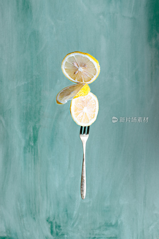 绿色背景叉子上叉着的新鲜水果柠檬片