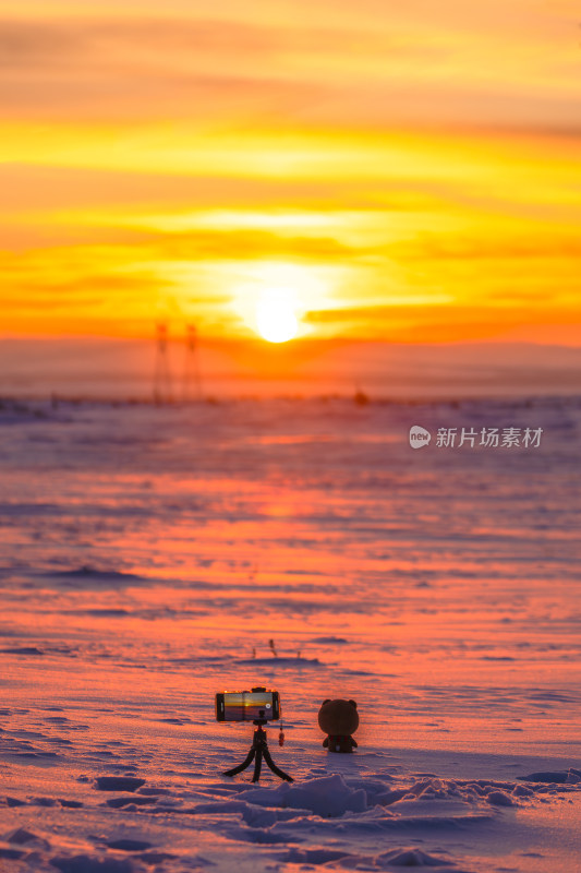 金色日落下的雪原，雪地里一台手机在拍摄