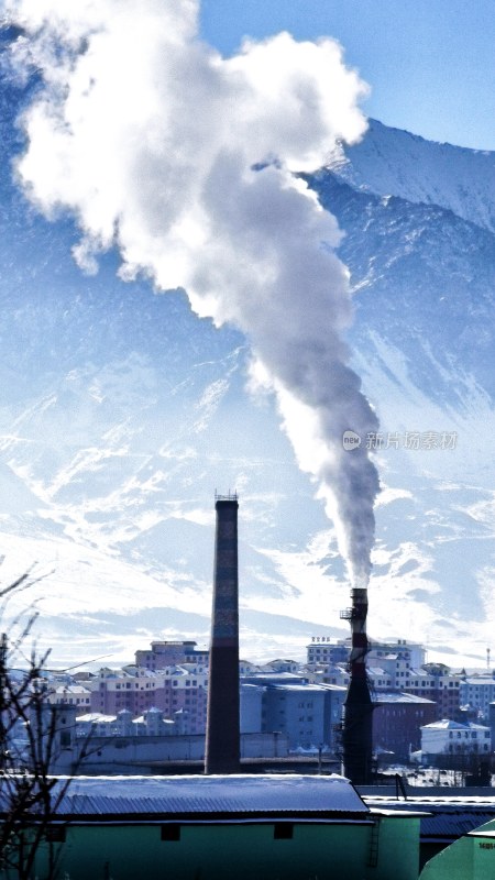 雪山下城市中烟囱正在排放烟雾的景象