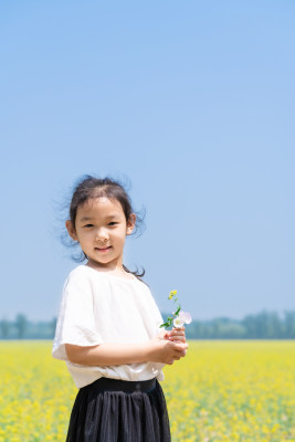 夏天站在油菜花田边拿着野花的女孩