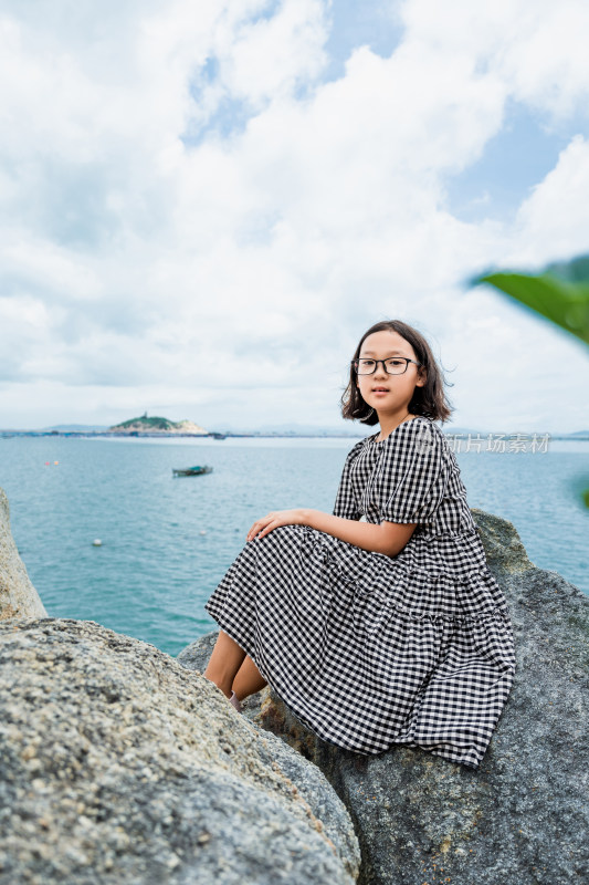 女孩坐海边岩石眺望远方