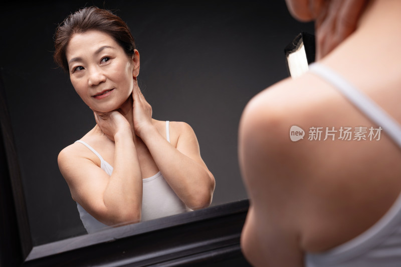 优雅的中年女人对着镜子做颈部护理