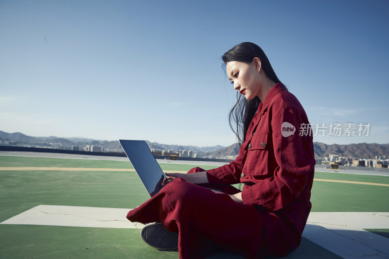 亚洲商务年轻女性在楼顶停机坪使用电脑办公