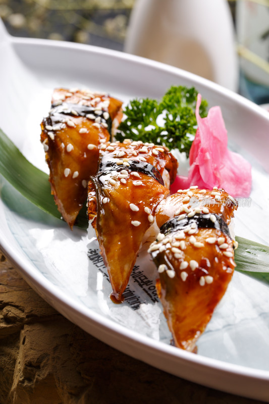 鹅颈白瓷盘装的烤鳗鱼手握寿司摆放在石头上