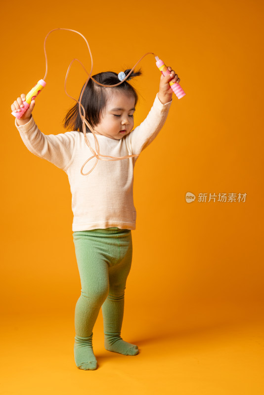 在黄色背景前玩跳绳的中国女童