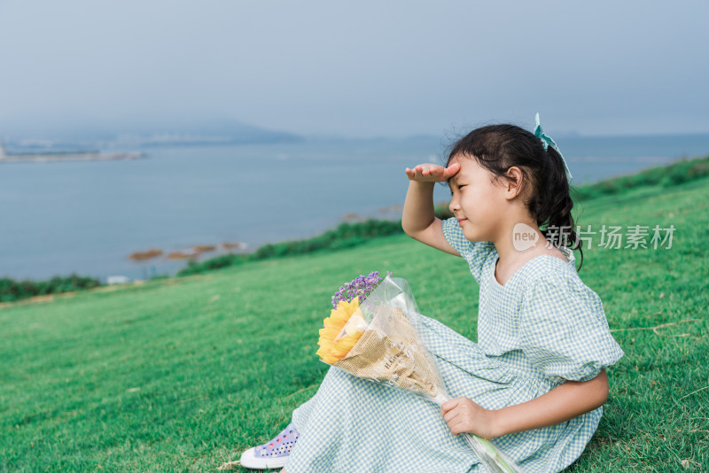 坐在山坡草地上眺望远方大海的女孩