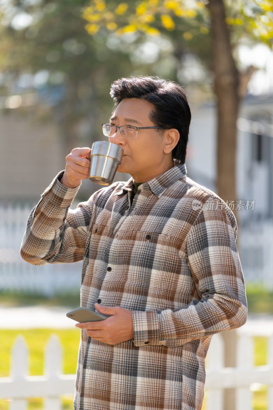 一个老年男人站在露营院子里拿着手机喝咖啡