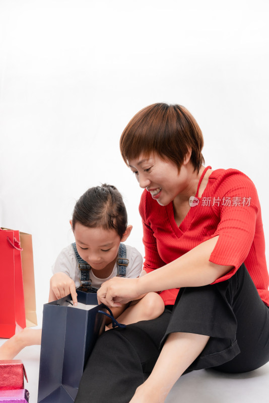 坐在白色背景前拆开礼物的中国籍母女