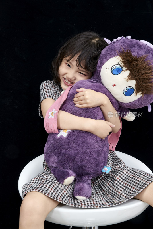 黑色背景里坐在凳子上抱着娃娃玩耍的可爱亚洲小女孩（儿童）