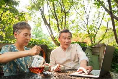 老年夫妇坐在院子里使用笔记本电脑