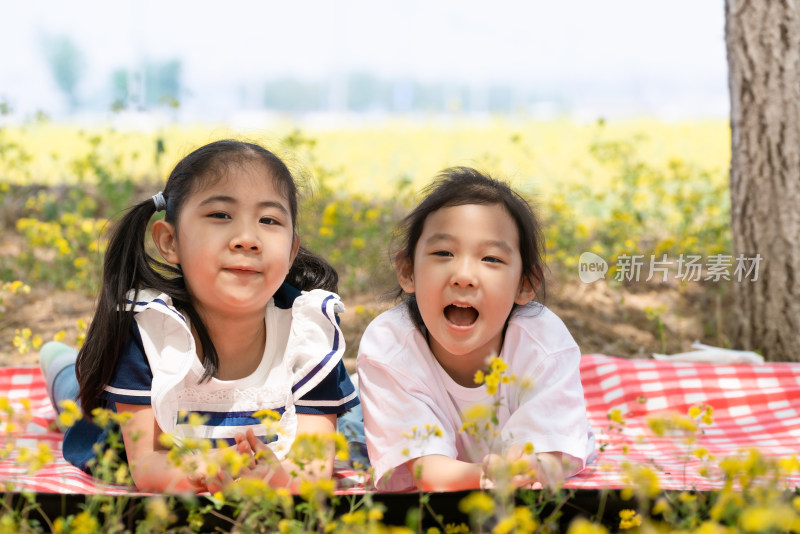 两个趴在油菜花田边野餐垫上的女孩