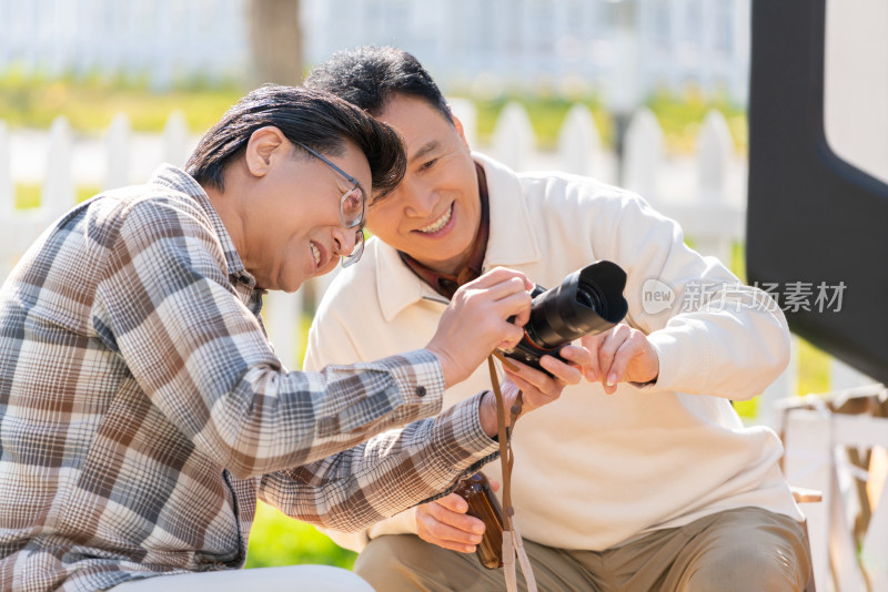 两个老年男人坐在露营地看数码相机