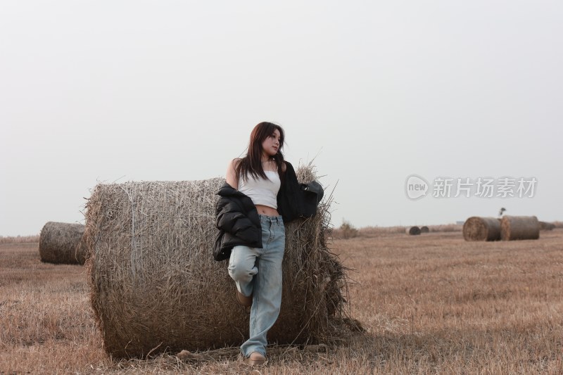 女子倚靠草垛于田野中