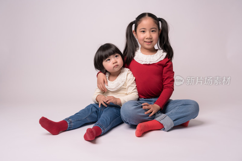 两个中国籍女童坐在白色背景前