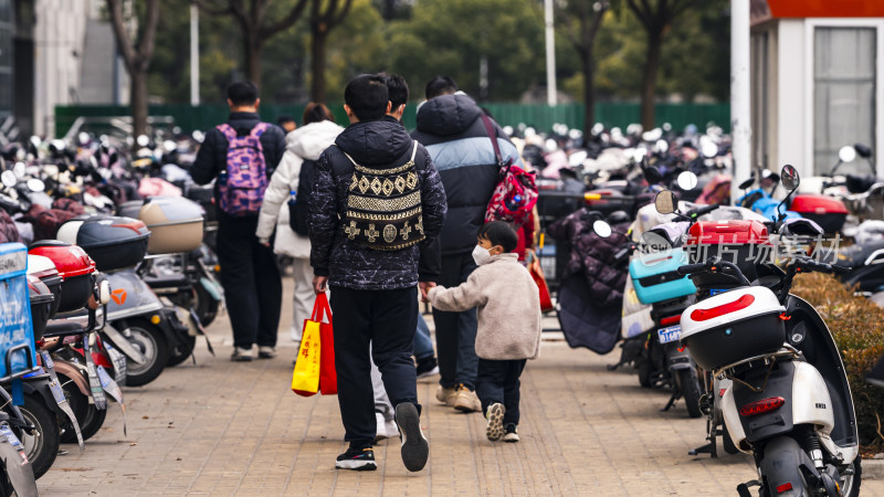 人行道上大人牵小孩走过停满的电动车