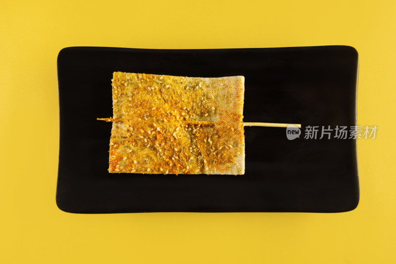 黄色背景中黑色盘子里的炸豆腐干