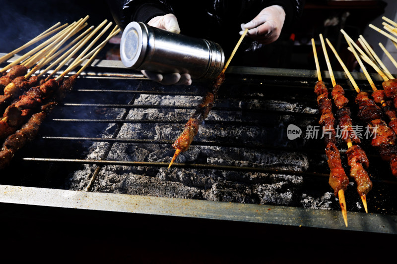 戴手套的手在烤架上撒调料烤羊肉串特写