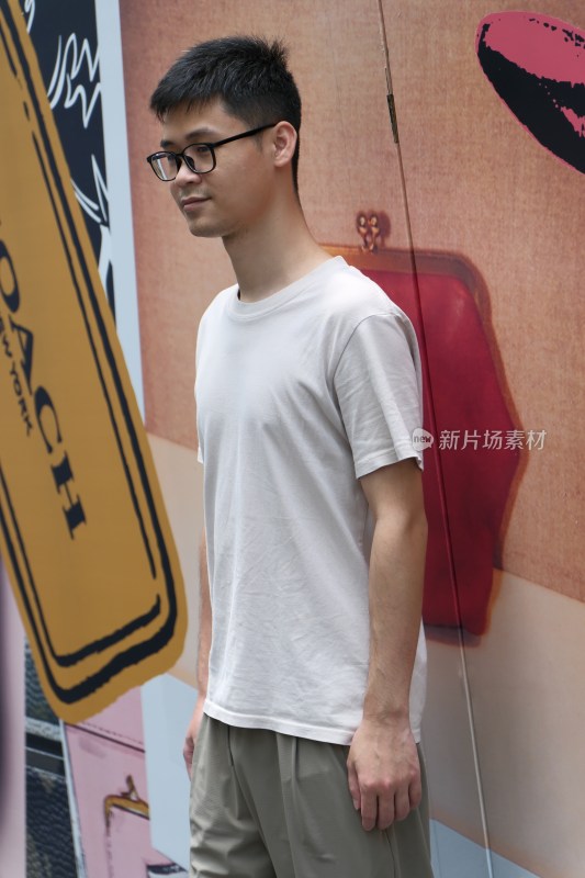 戴眼镜男士站立在广告墙前