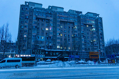 雪天夜晚亮灯的居民楼外景马路街道