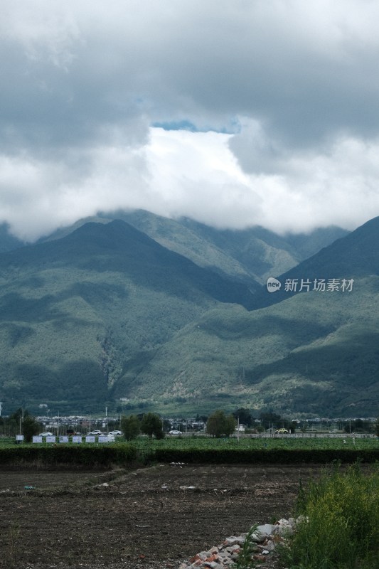 阴云下的青山远景及山脚下的土地