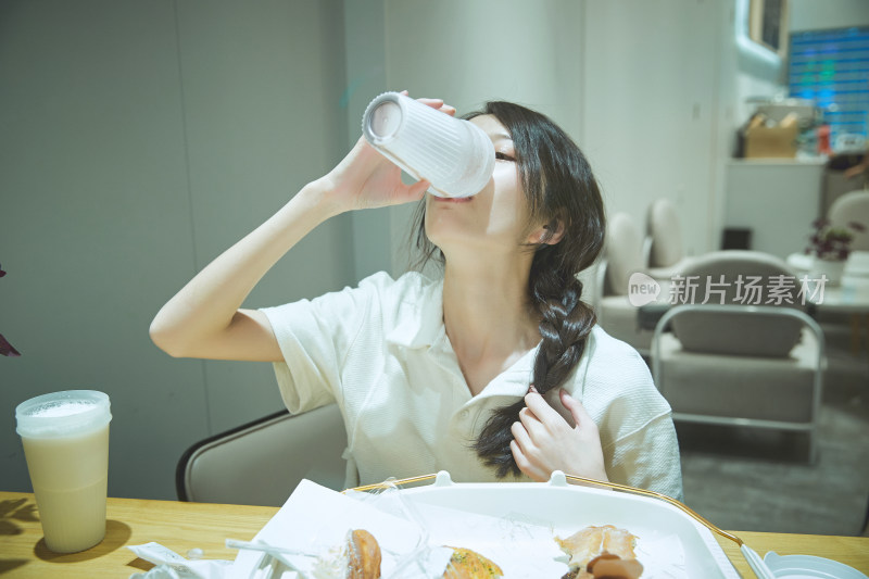 在烘焙店吃面包喝牛奶的可爱亚洲少女