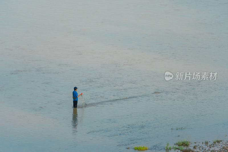 一人站在浅水中撒网捕鱼的画面