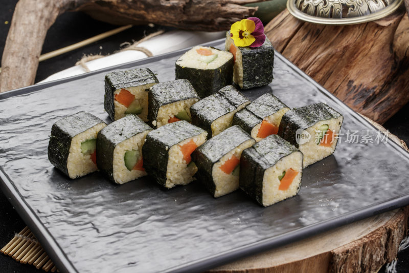 黑色石盘装的小米寿司卷摆放在樟木砧板上