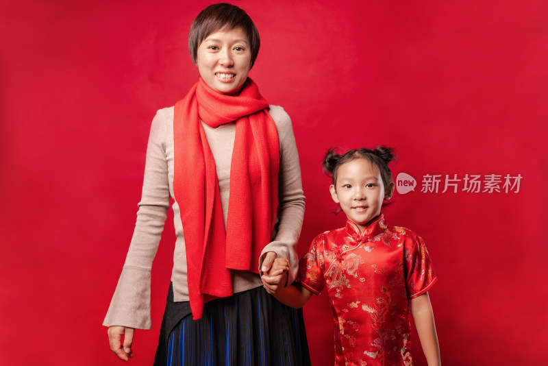 牵着手站在红色背景前的中国母女