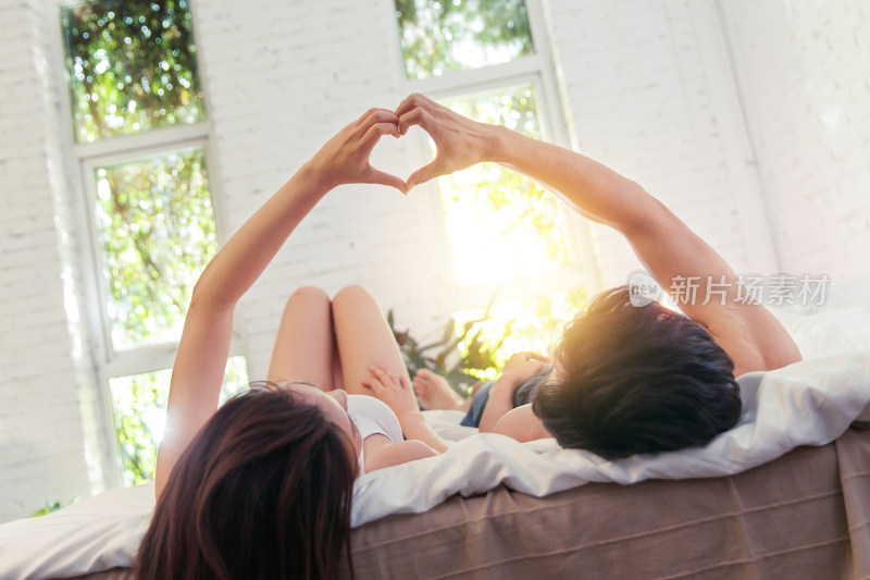 快乐的年轻情侣躺在床上做心形手势