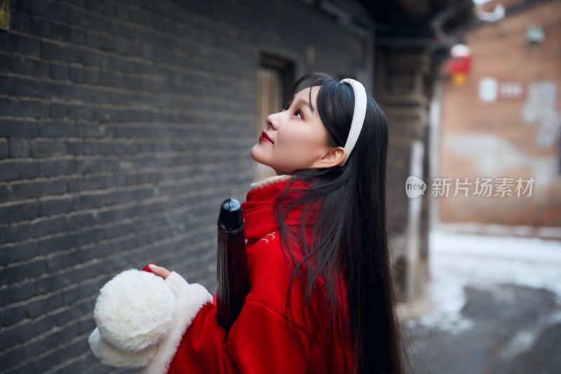 雪后在老城古巷穿着喜庆服饰的亚洲少女