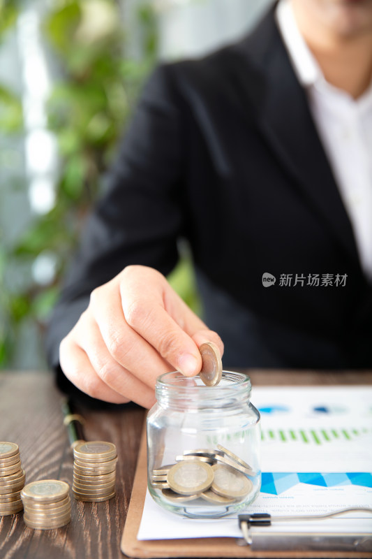 手拿欧元硬币放入金融资料上的玻璃瓶中