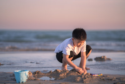 一个小男孩在夕阳下的海边的沙滩上挖沙子