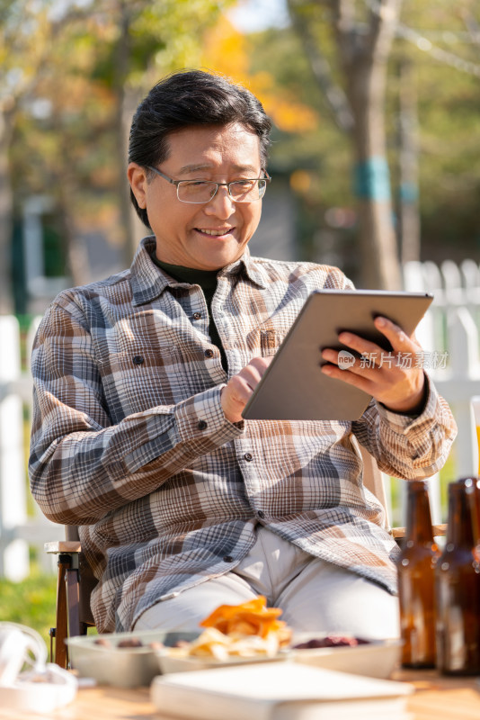 一个老年男人坐在露营院子里看平板电脑