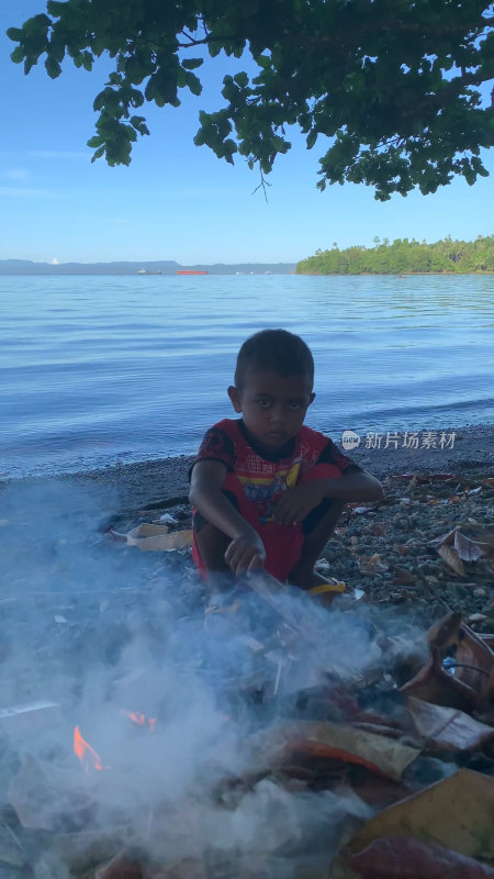 印尼当地小男孩在海边沙滩上生火