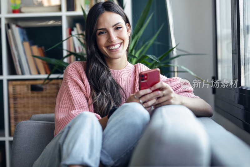 女子室内沙发上玩手机微笑