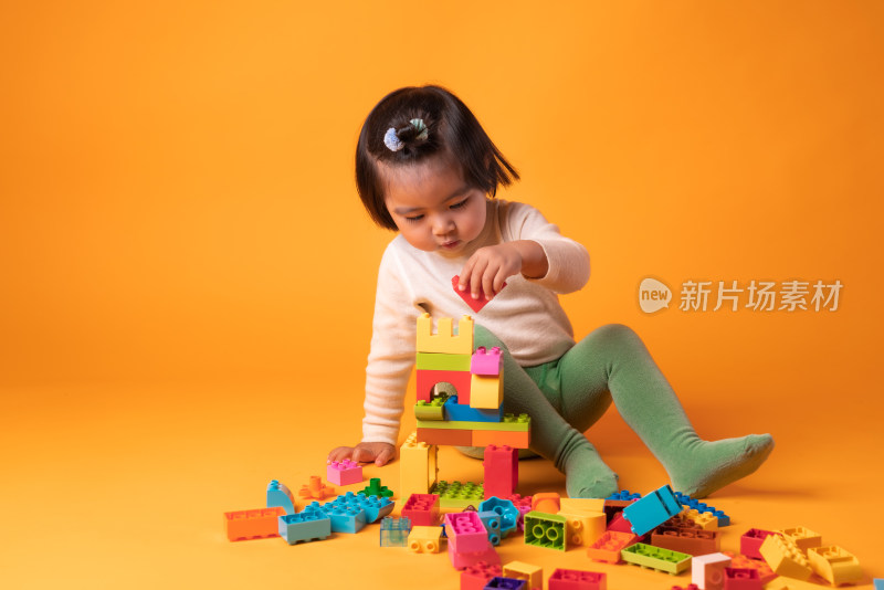 坐在黄色背景前玩积木的中国女童