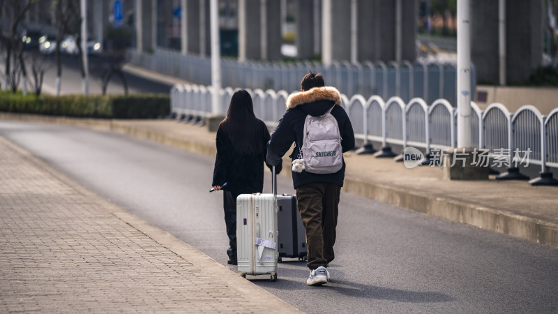 两人拖着行李箱走在户外道路上