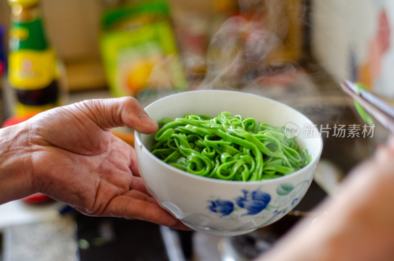 从锅里盛出一碗绿色蔬菜面条