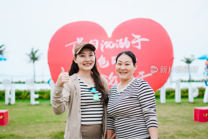 在草地上红色心形气球前开心拍照的亚洲母女